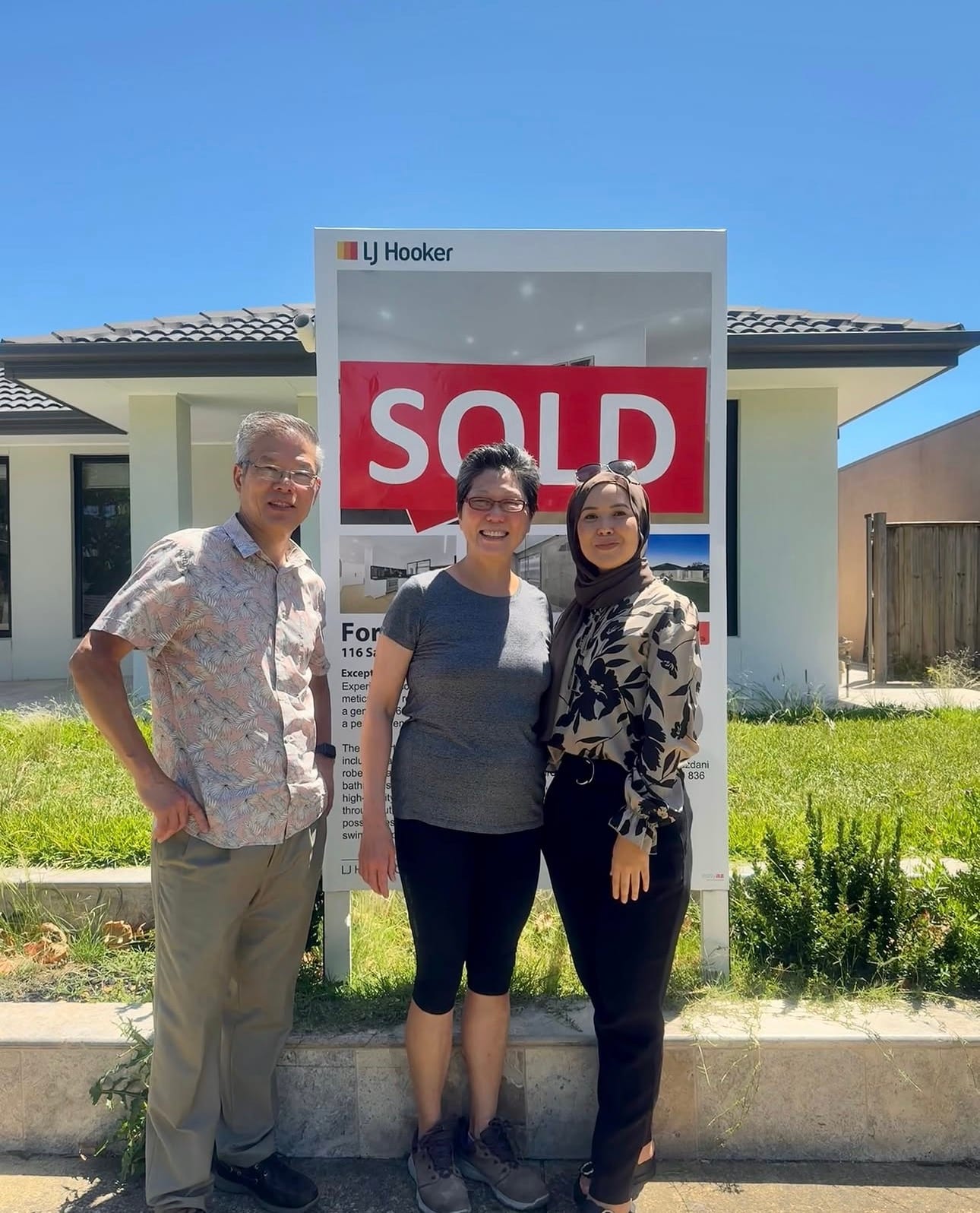 Fatima handing a settlement gift to a happy client beside an LJ Hooker Casey SOLD board.