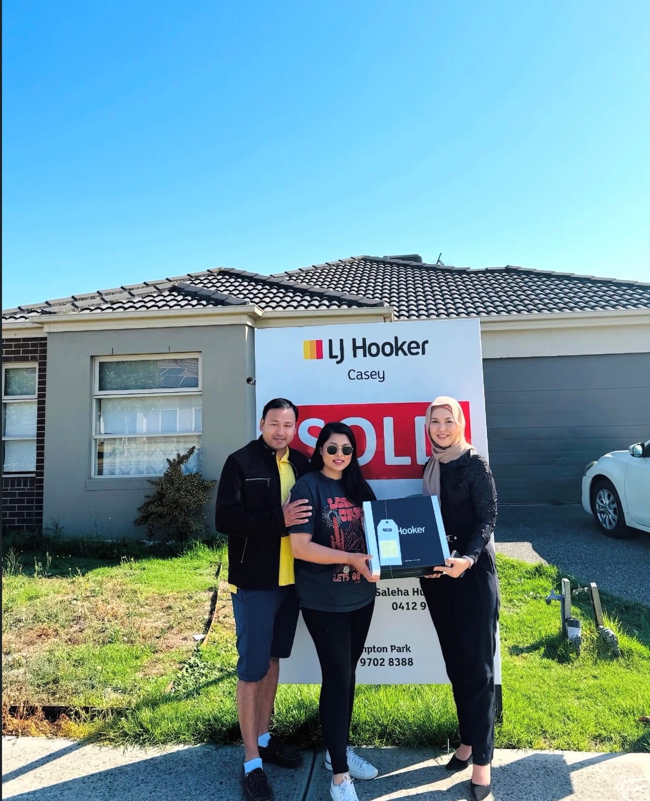 A family celebrating their sale with Fatima in front of a SOLD board.