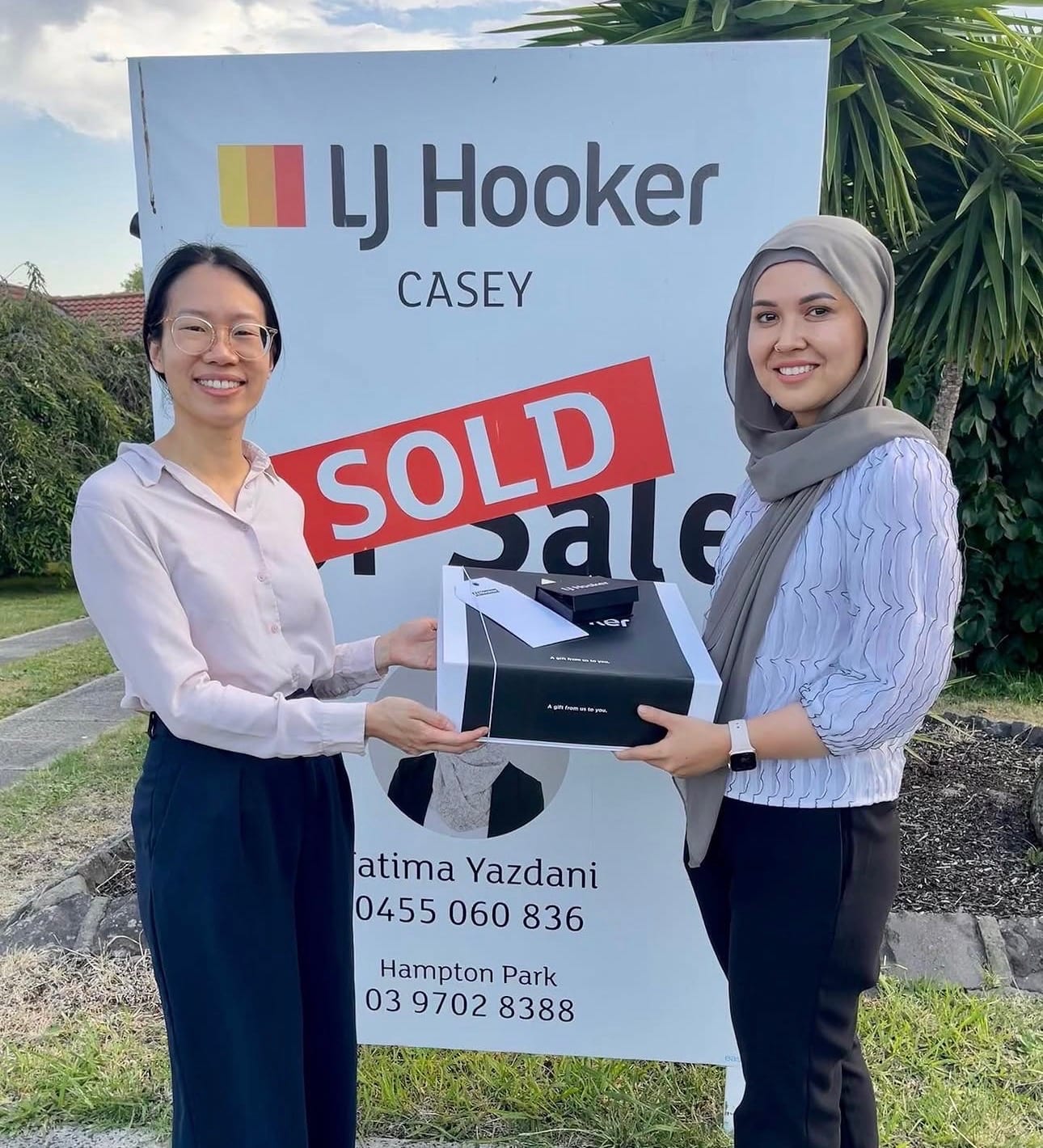 Fatima Yazdani handing a gift to a happy client beside an LJ Hooker Casey SOLD board.